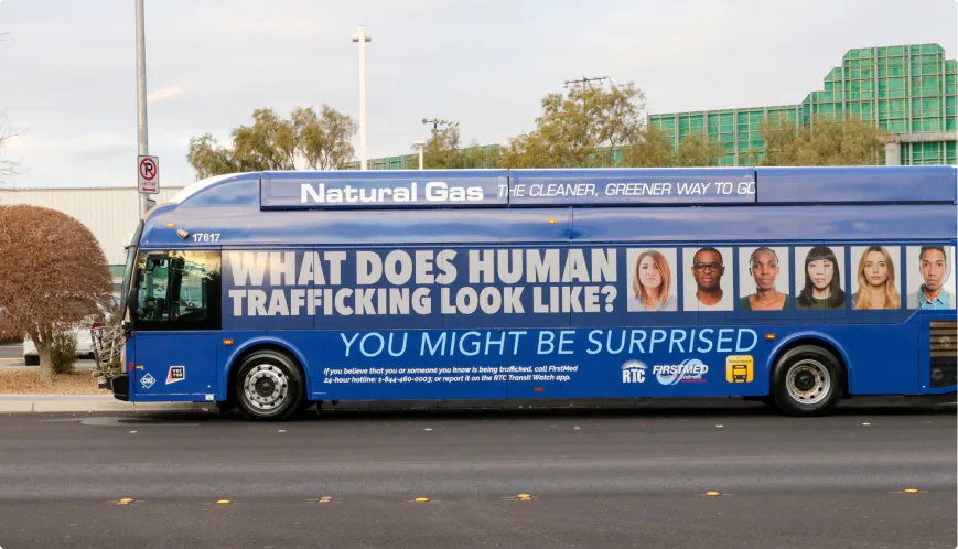 A blue city bus with a large ad reading What does human trafficking look like? You might be surprised above photos of diverse people, promoting awareness and a human trafficking hotline.