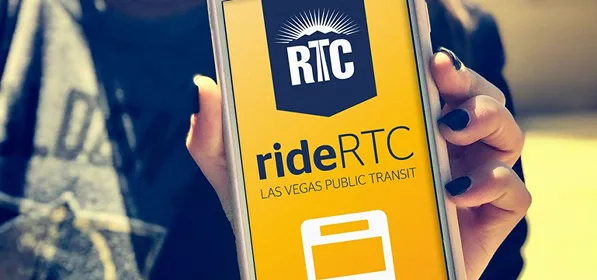 A person holds a smartphone displaying the yellow rideRTC Las Vegas public transit app screen, featuring the RTC logo and a bus icon.