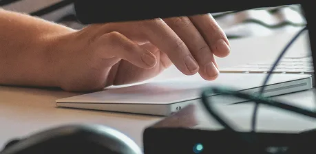 A close-up of a hand resting on a touchpad or trackpad next to a keyboard, with some electronic devices and cables partially visible in the foreground.