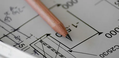 A sharpened pencil rests on top of an architectural blueprint, featuring detailed measurements, lines, and annotations related to a construction or engineering project.