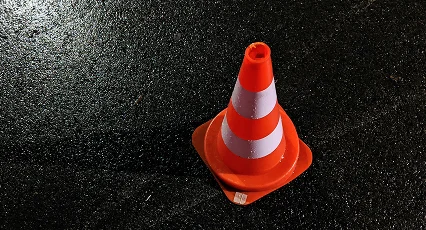 A single orange and white traffic cone stands on wet, black pavement, reflecting light from above.