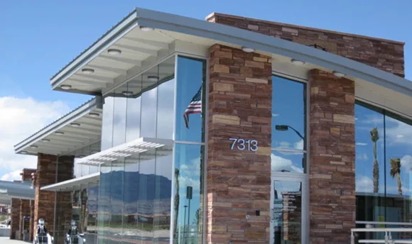 Modern building with large glass windows and brick accents, reflecting the sky and palm trees. An American flag is visible inside. The number 7313 is displayed on the buildings exterior.