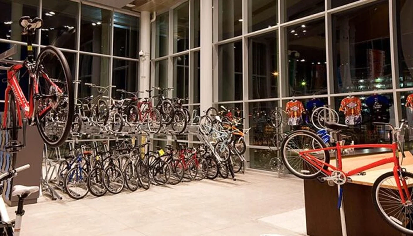 A modern bicycle shop interior with large windows, racks of bicycles displayed neatly, and several cycling jerseys hanging on the wall. The space is well-lit and orderly.
