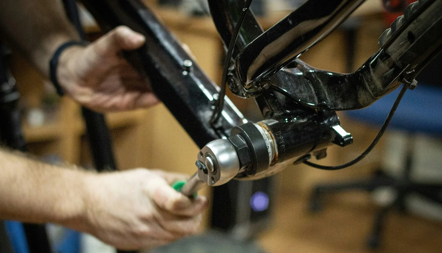 A person uses a tool to adjust or install the bottom bracket on a black bicycle frame, focusing on the mechanical components and hands during bike maintenance.